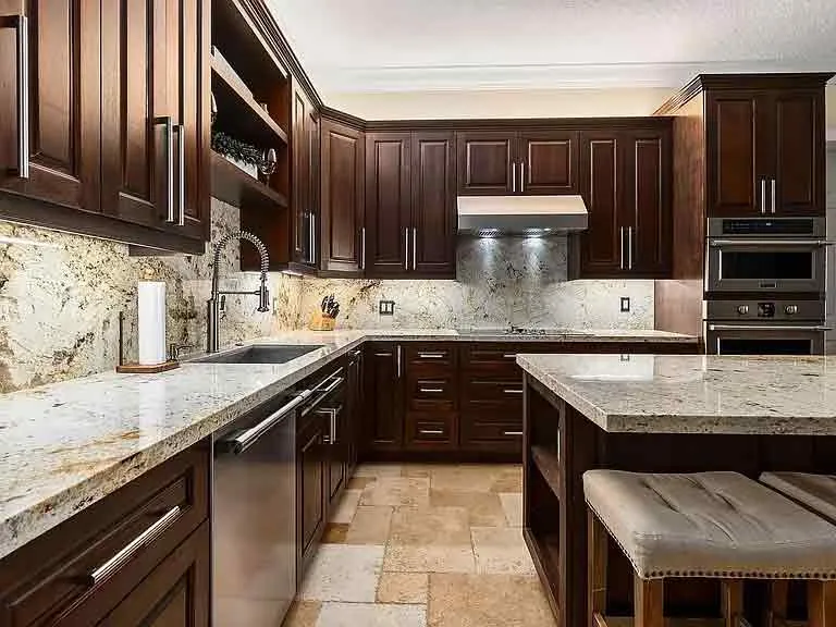 Modern kitchen with dark wooden cabinets, light granite countertops, stainless steel appliances, under-cabinet lighting, a center island with seating, beige tile flooring, and expertly crafted cabinets featuring hidden damage repair.