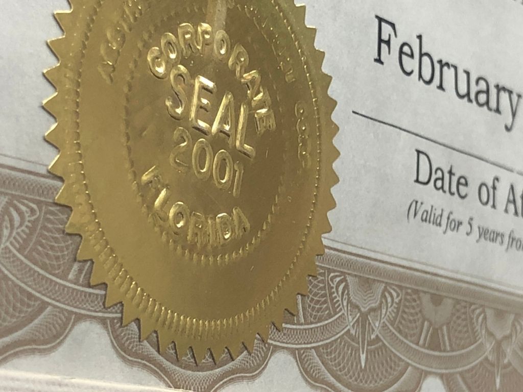 Close-up of a gold embossed corporate seal labeled CORPORATE SEAL 2007 FLORIDA on a certificate. The certificate text includes February and Date of A with decorative borders visible.