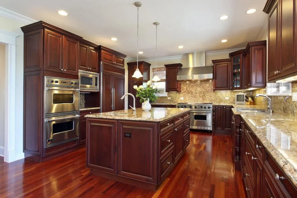 Spacious kitchen with dark wood cabinets, stainless steel appliances, granite countertops, a large island with a flower vase, pendant lights, polished wood flooring, and expert cabinet repair to address any hidden damage.