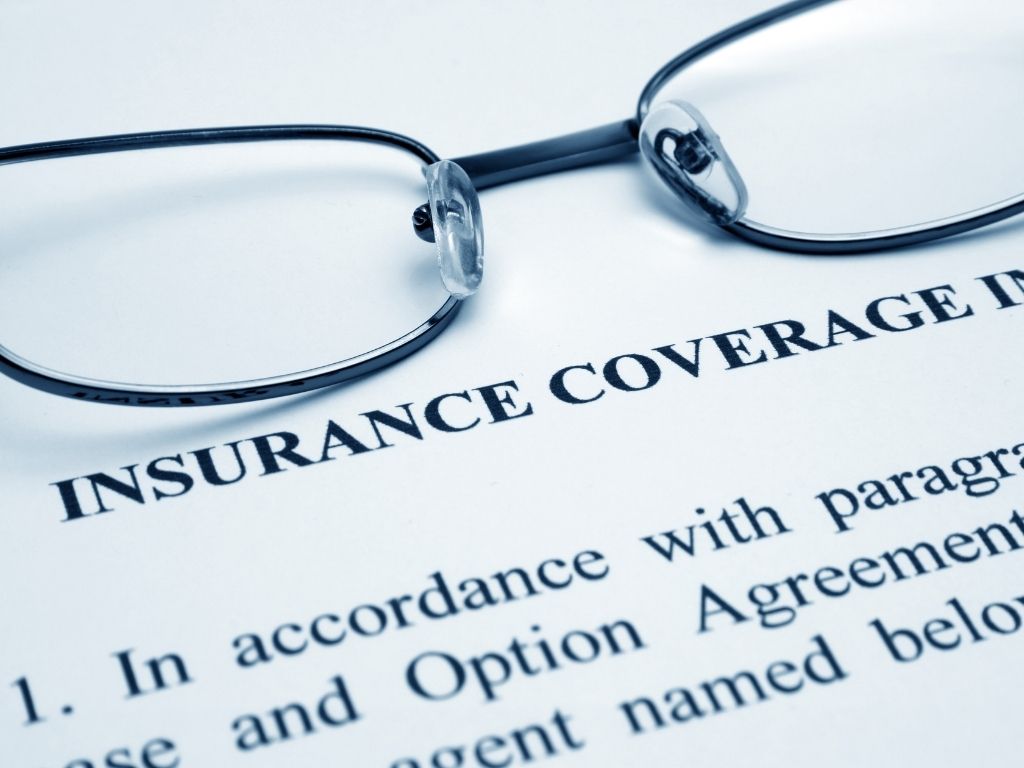 A pair of eyeglasses rests on a document titled INSURANCE COVERAGE, with text and paragraphs partially visible beneath the glasses—hinting at important details on Homeowners Insurance and Water Damage Restoration in Marion, Illinois.